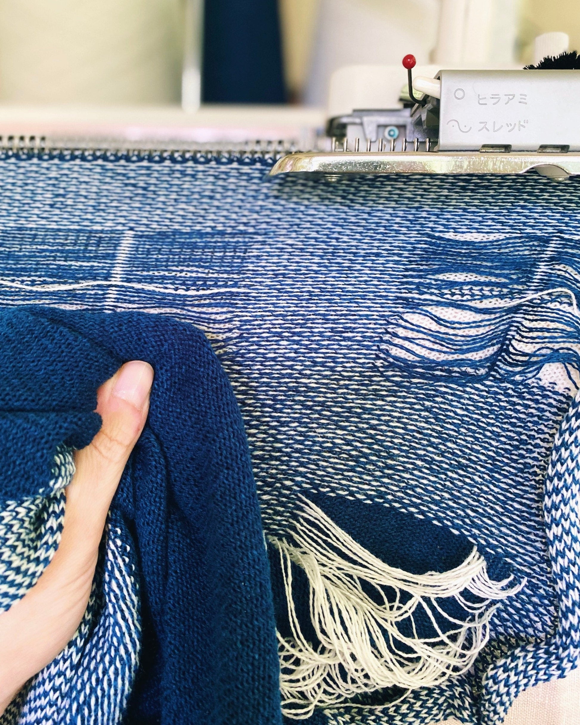 Hand holding blue fabric next to a loom with blue and white patterned fabric.