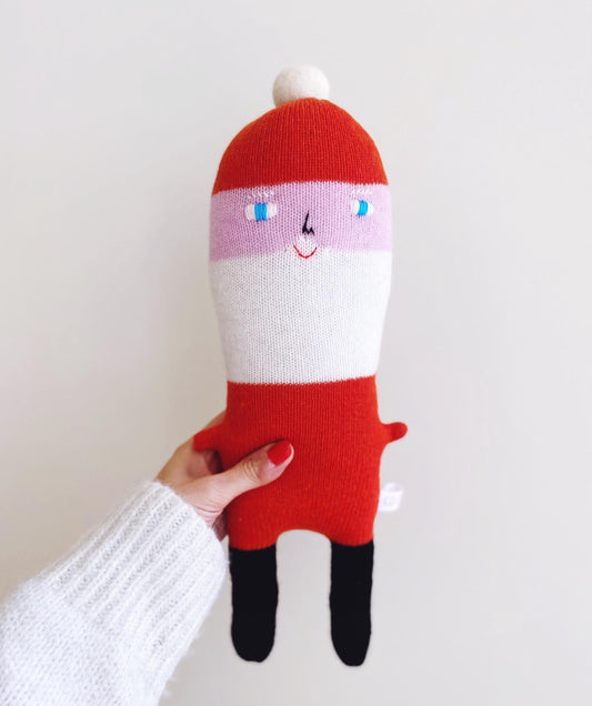 Hand holding a red and white santa plush toy with a smiling face on a plain background