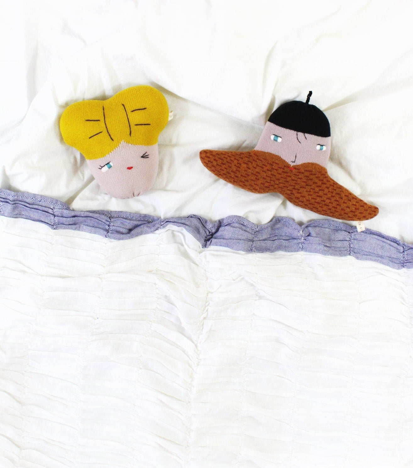 Two plush toys, one with yellow hair and pink face, the other with a brown mustache beard and pink face, lying on a white surface.