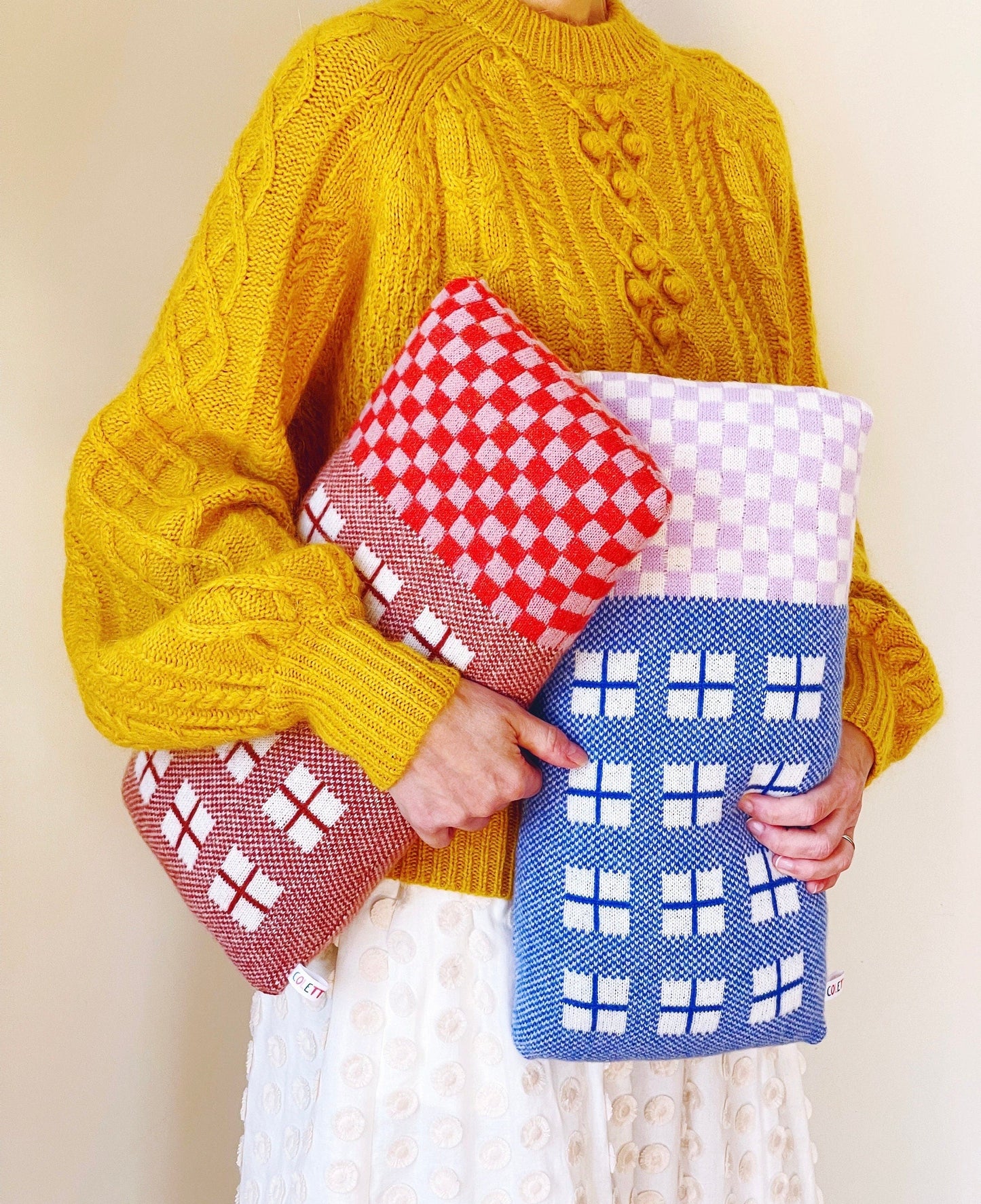 Person wearing a yellow sweater holding two knitted house-shaped pillows.