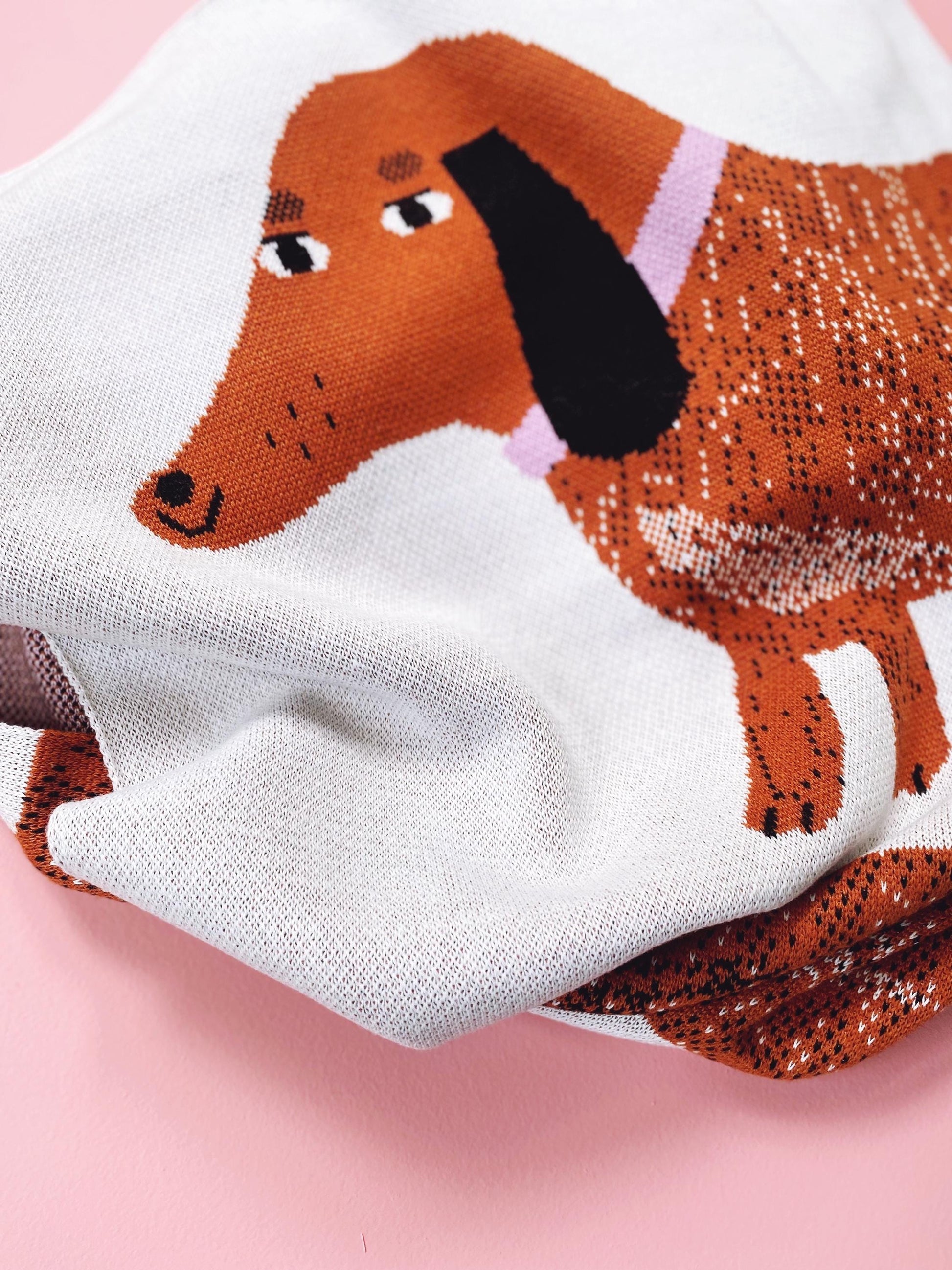 Sausage dog design on a knit blanket on a pink background