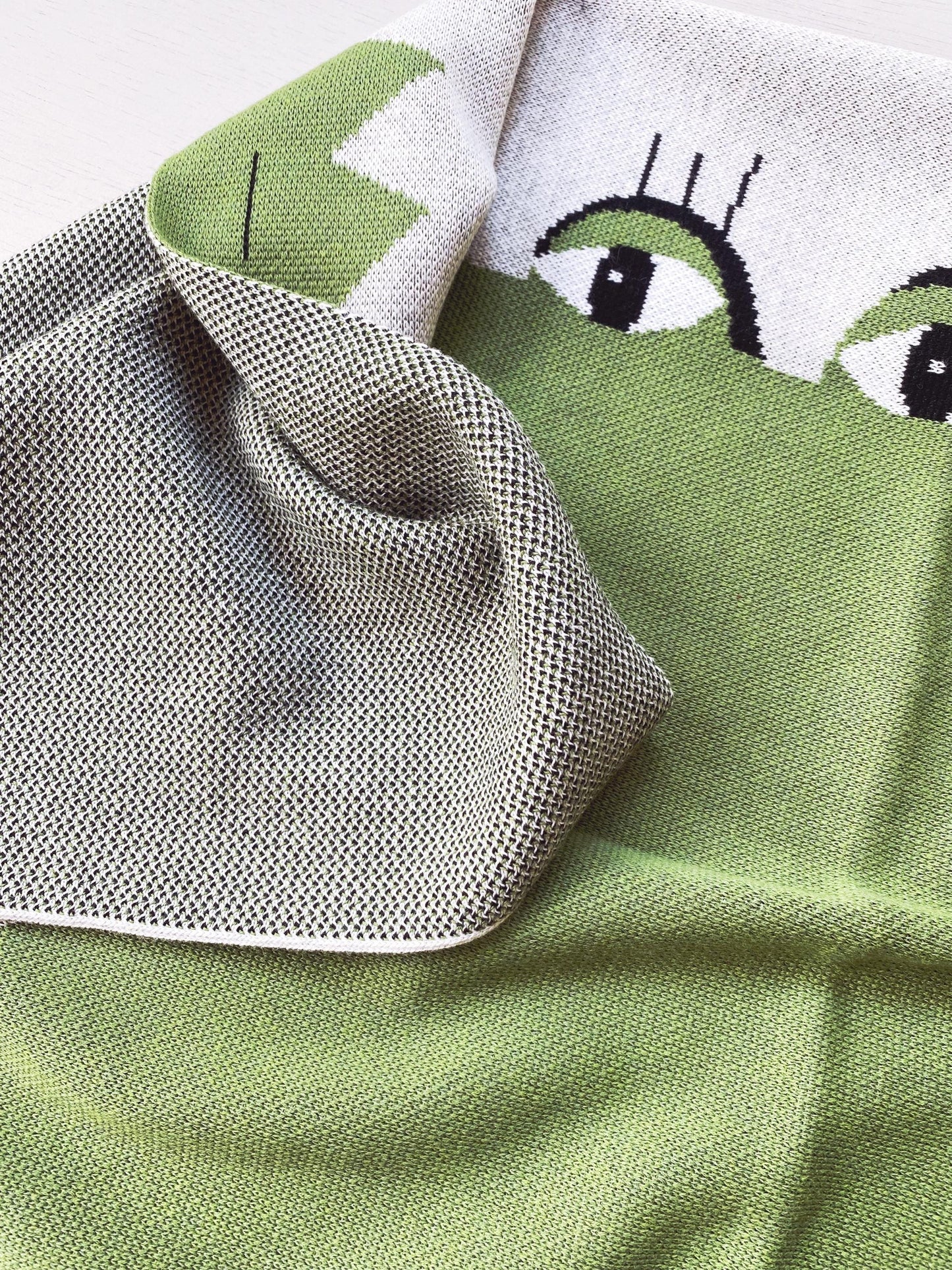 Close-up of a knit fabric with a green alligator design on a white background