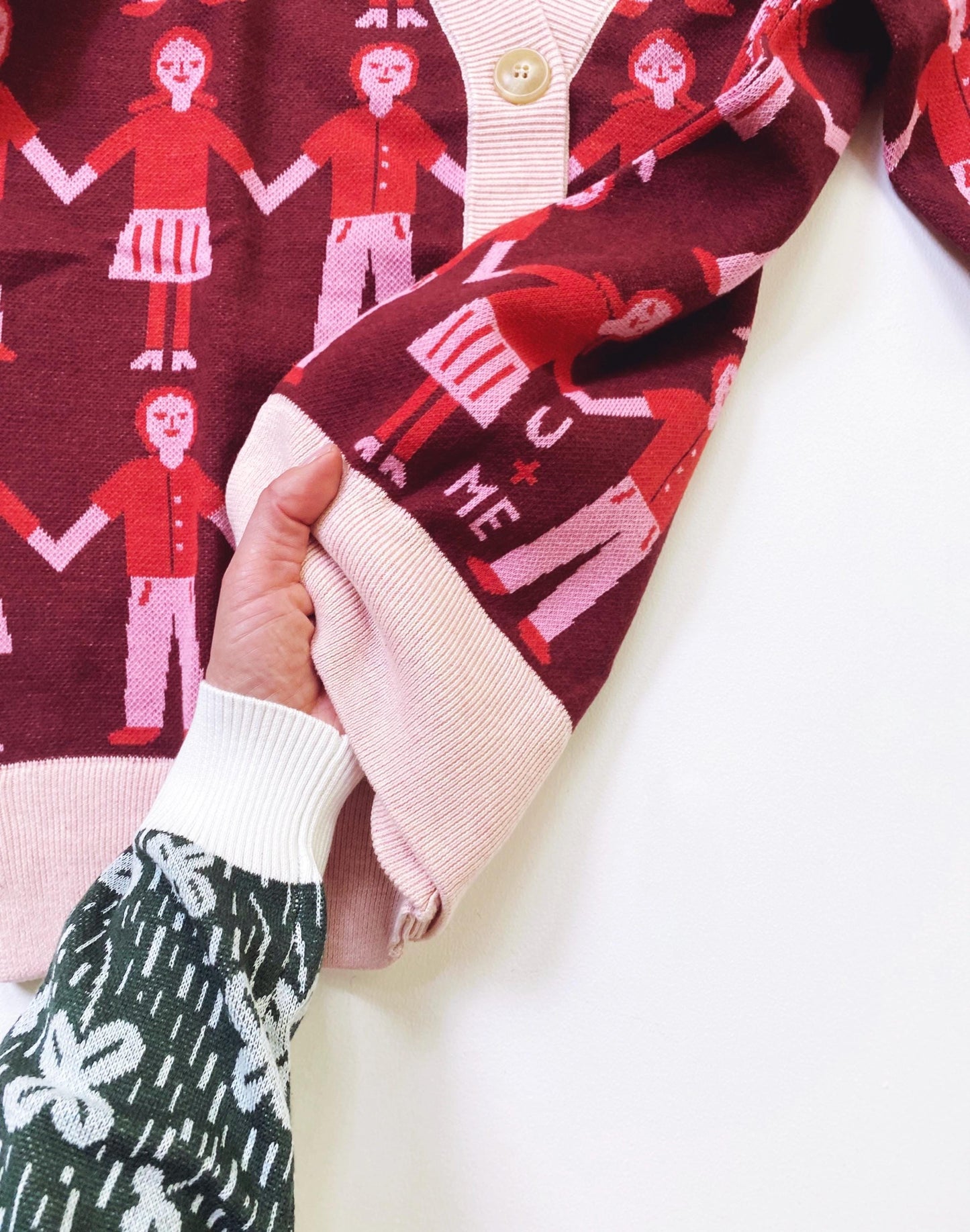 Close-up of a sweater cardigan with a pattern of people holding hands on a red background.