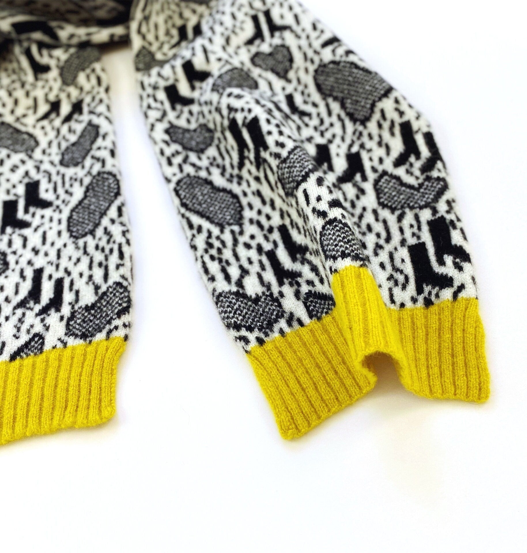 Knitted scarf with black and white pattern and yellow trim on a white background