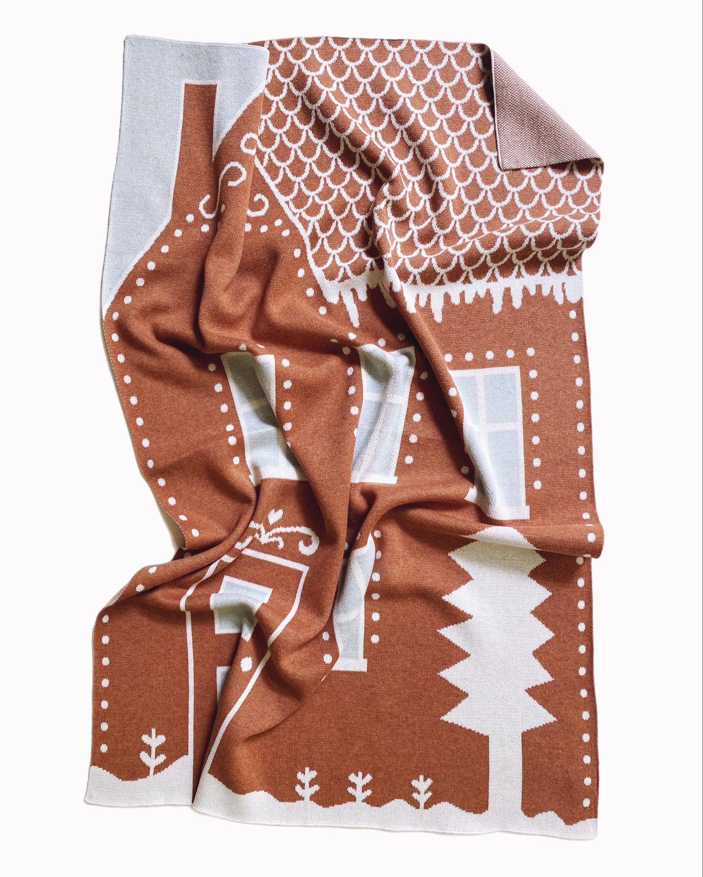 Knitted baby blanket with brown and white gingerbread house pattern on a white background