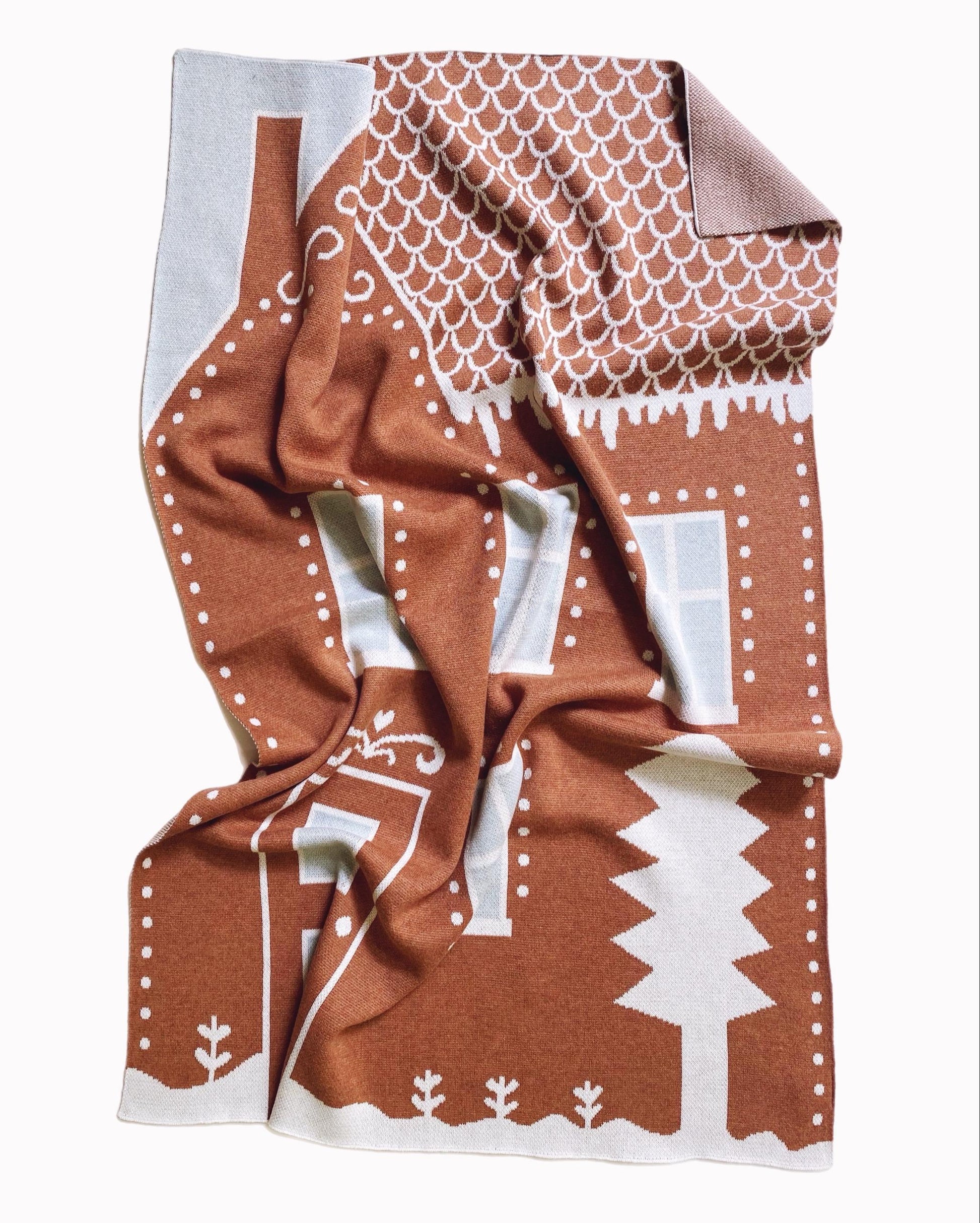 Knitted baby blanket with brown and white gingerbread house pattern on a white background