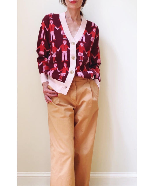 Person wearing a patterned cardigan and beige pants against a plain background