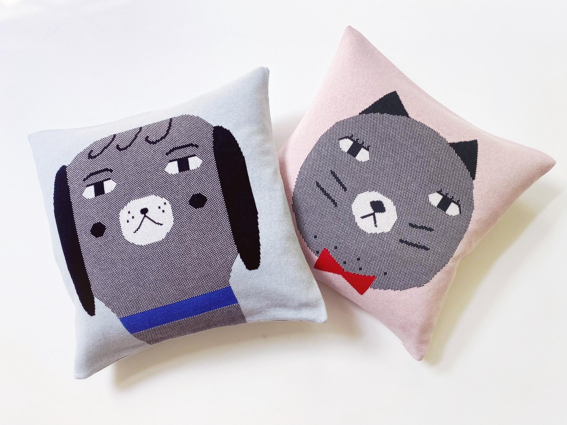 Two decorative knitted pillows with dog and cat faces on a light background