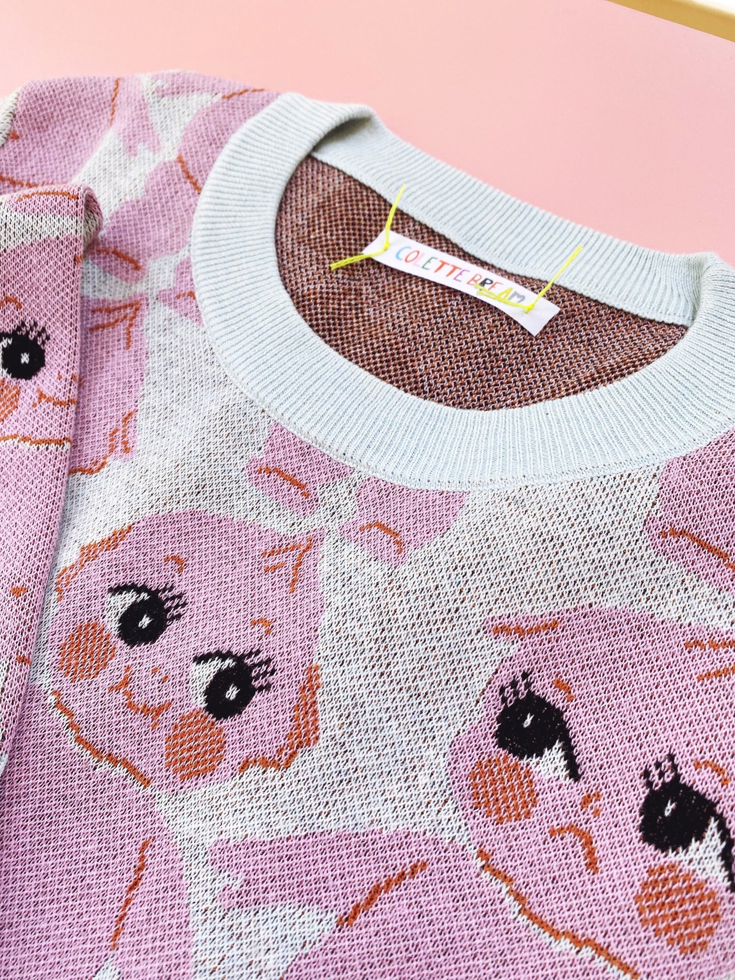 Pink knit sweater with cartoon kewpie doll character design on a pink background