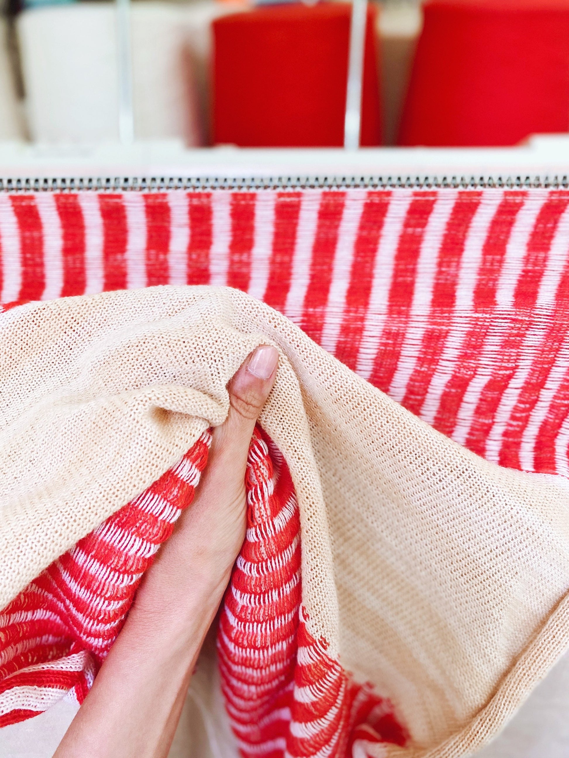 Close-up of a hand holding fabric with red and white striped pattern in the background