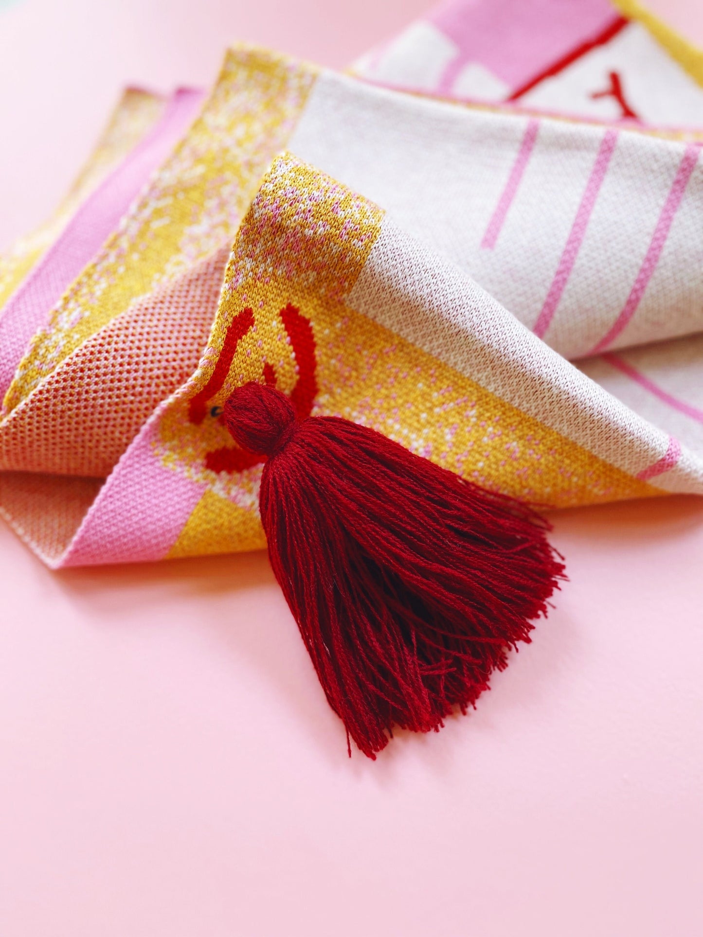 Colorful fabric with a red tassel on a pink background