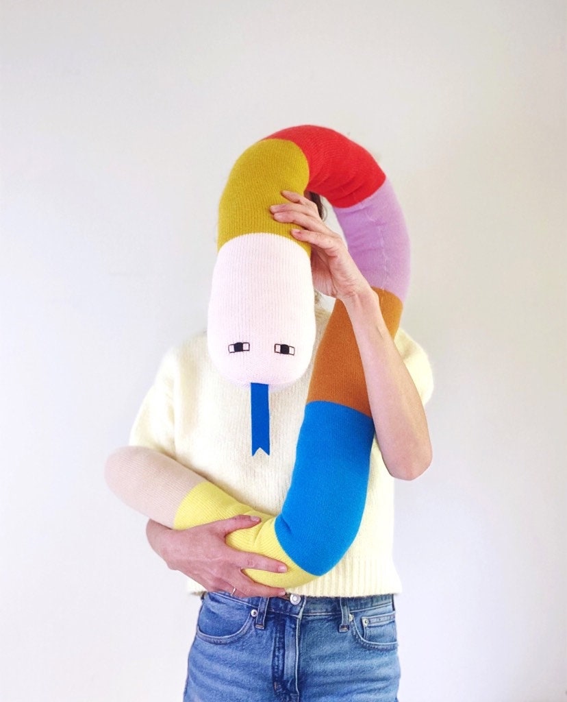 Person holding a colorful, knitted snake plush toy against a white background