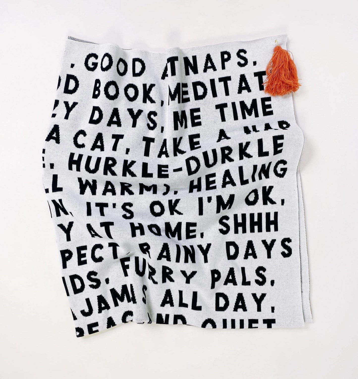 White knitted blanket throw with black text and a colorful tassel on a white background