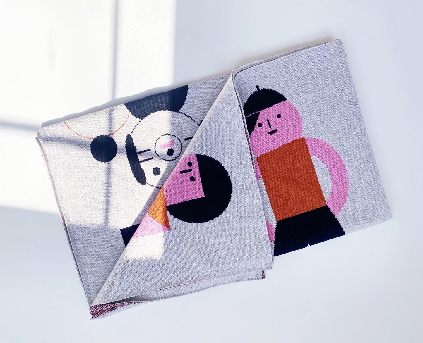 Folded knit blanket with modern geometric abstract character designs on a light background