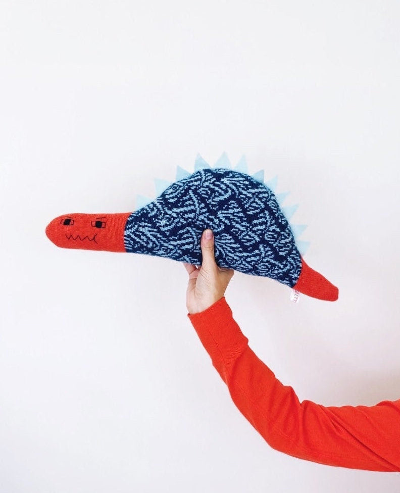 Hand holding a red and blue dinosaur toy with a textured surface against a white background