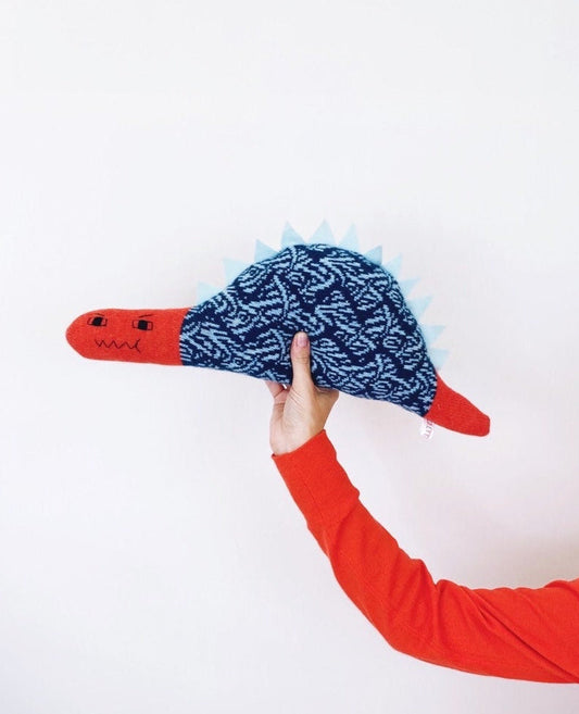 Hand holding a red and blue dinosaur toy with a textured surface against a white background