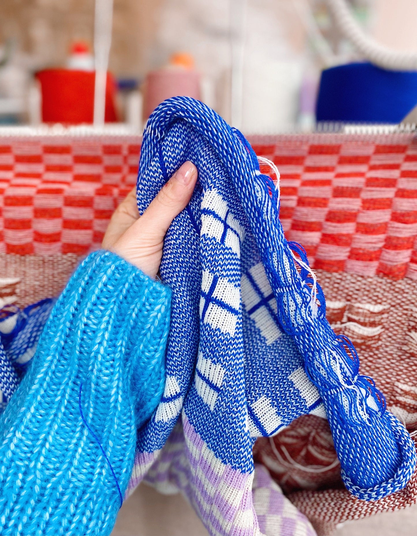 Person holding a blue and white patterned knitted fabric with a blurred background
