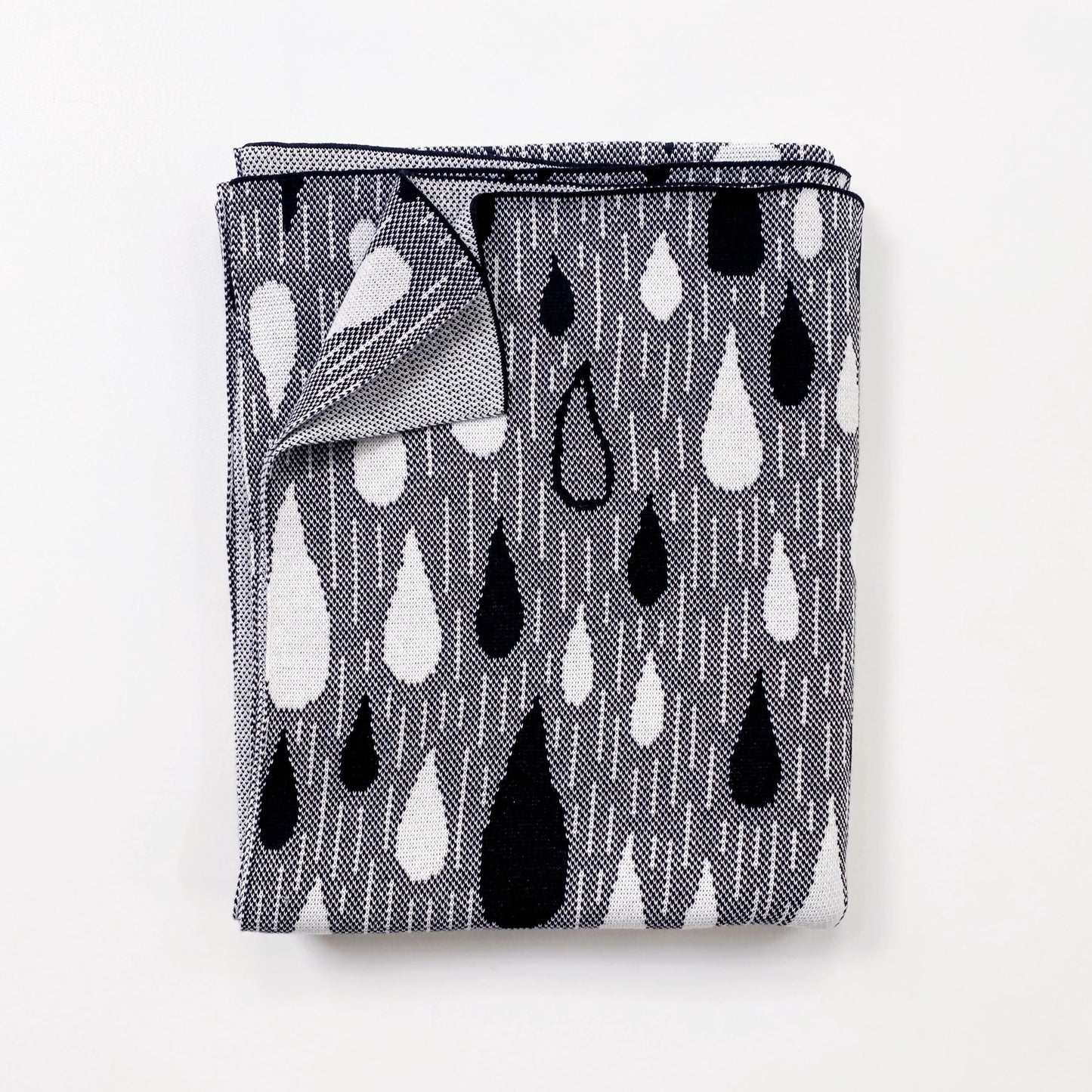 Folded black and white knitted blanket patterned with a raindrop design on a white background