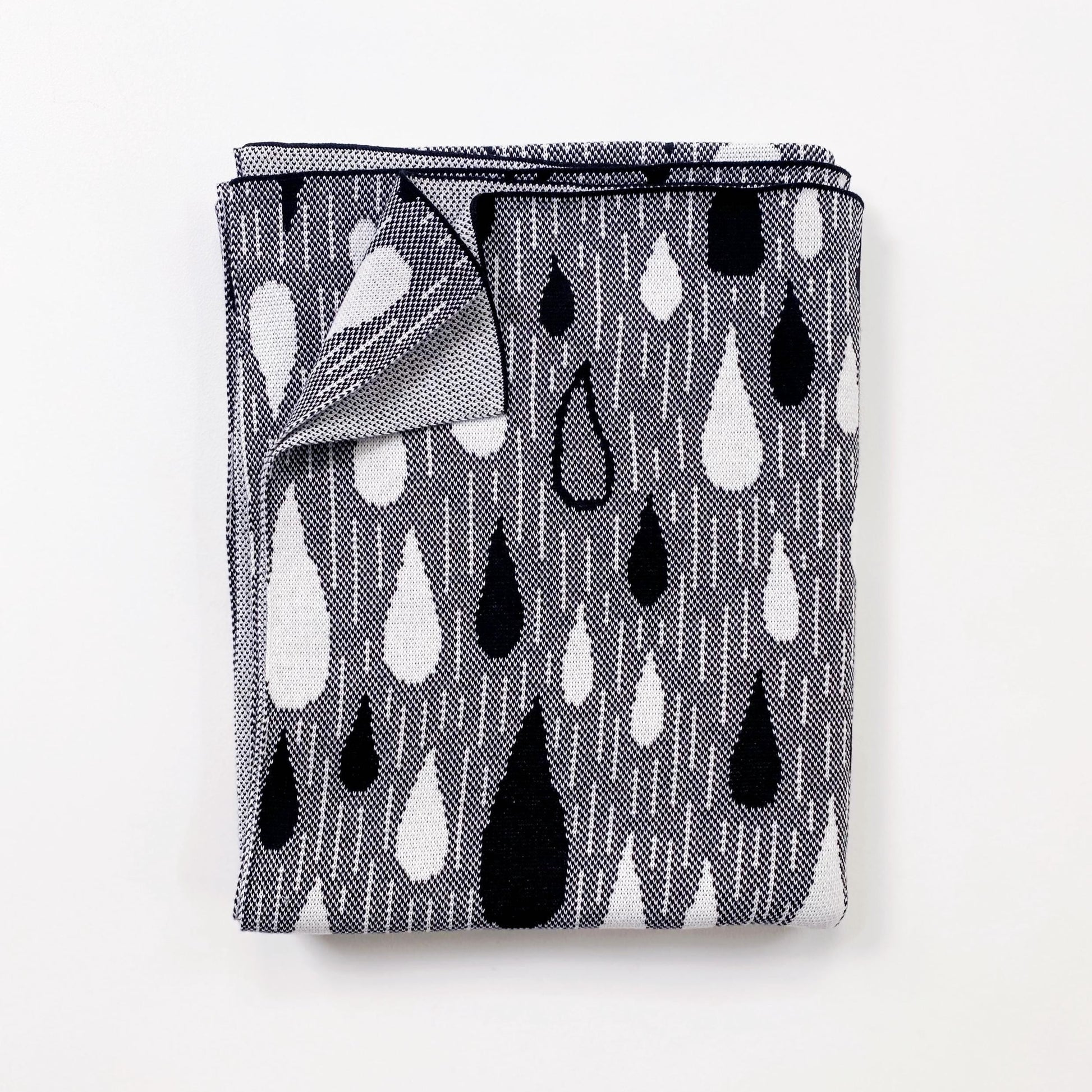 Folded black and white knitted blanket patterned with a raindrop design on a white background