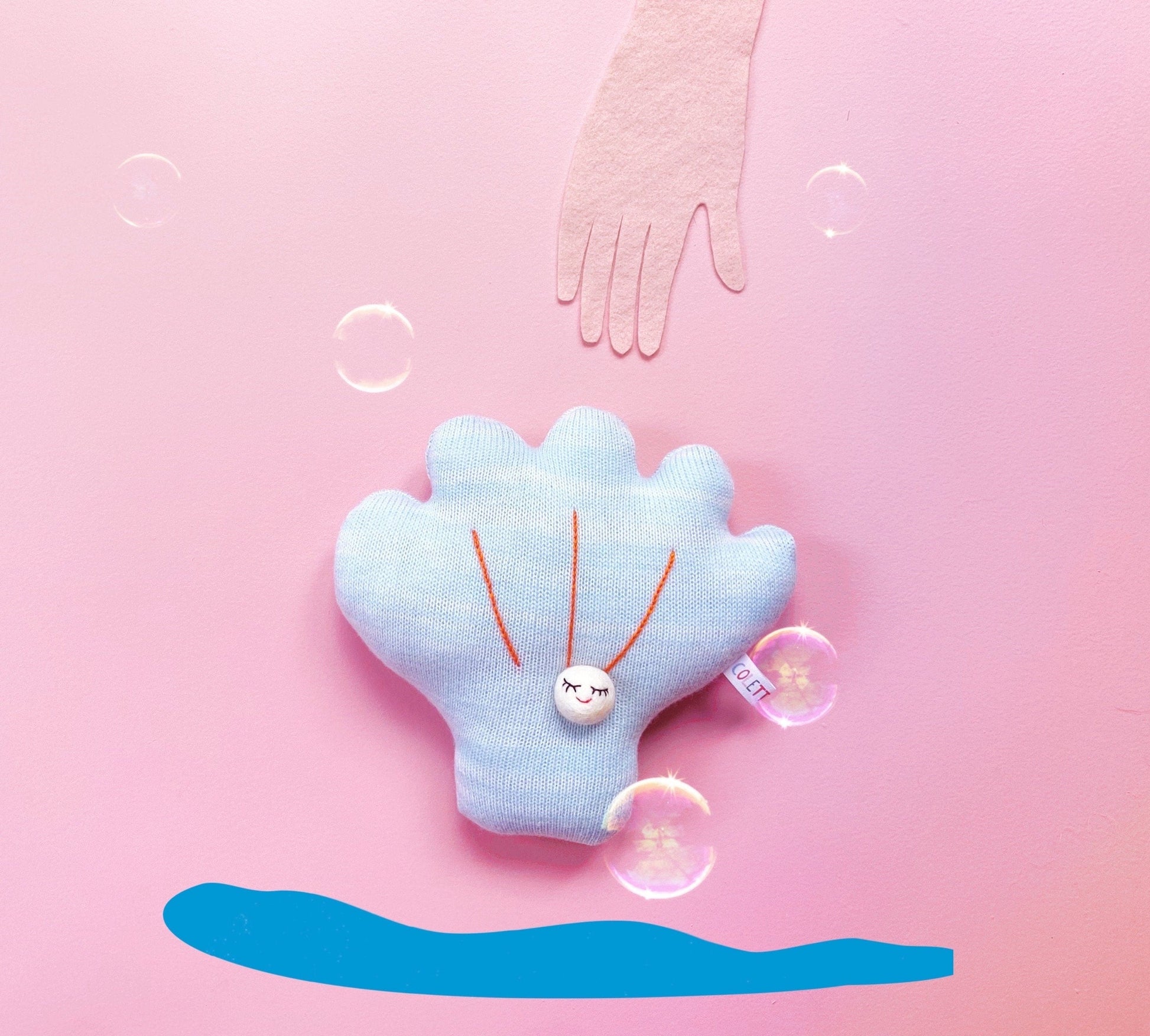 Blue shell-shaped knitted plush toy with a pearl on a pink background