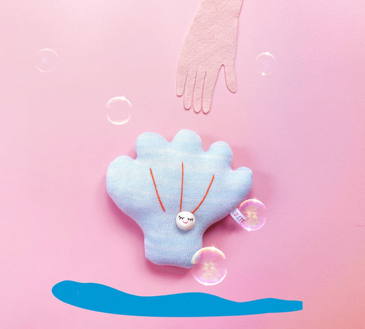 Blue shell-shaped knitted plush toy with a pearl on a pink background