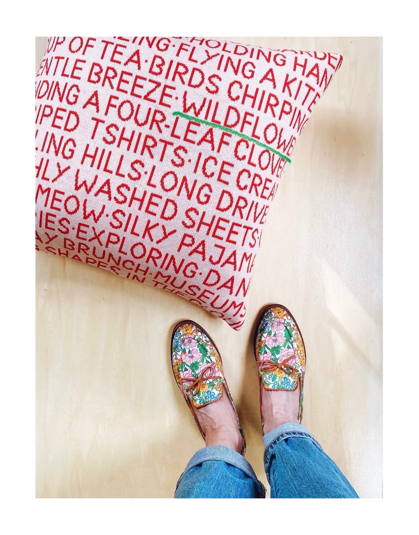 Floral shoes worn on a wooden floor with a colorful text-patterned rug.