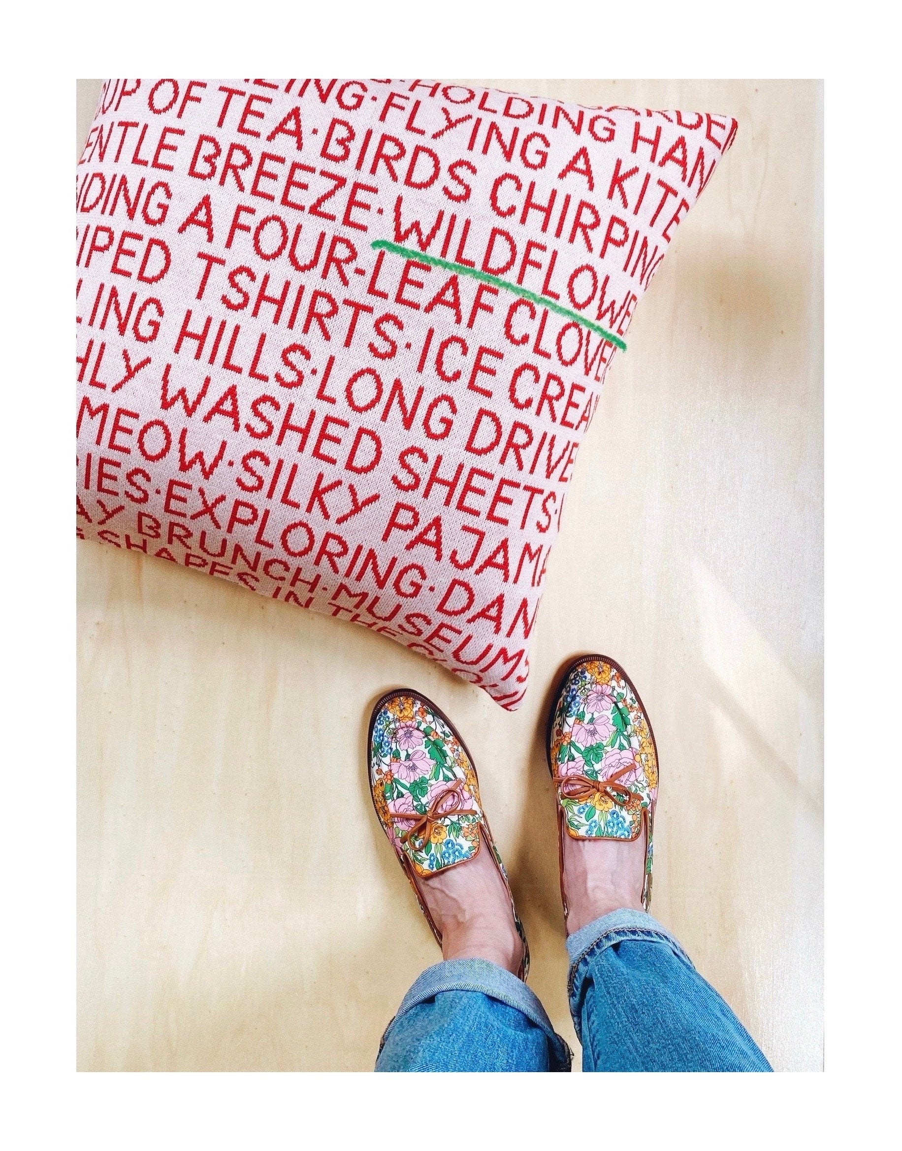 Floral shoes worn on a wooden floor with a colorful text-patterned rug.