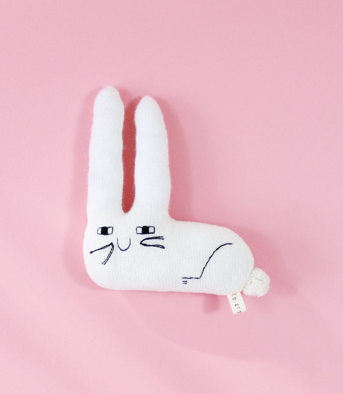 White rabbit-shaped knitted plush toy on a pink background