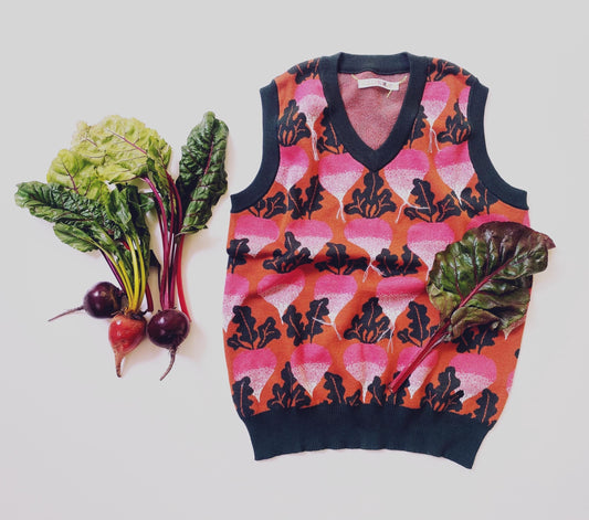 Colorful patterned knit vest with leaf design next to leafy greens, beets and radishes on a white background