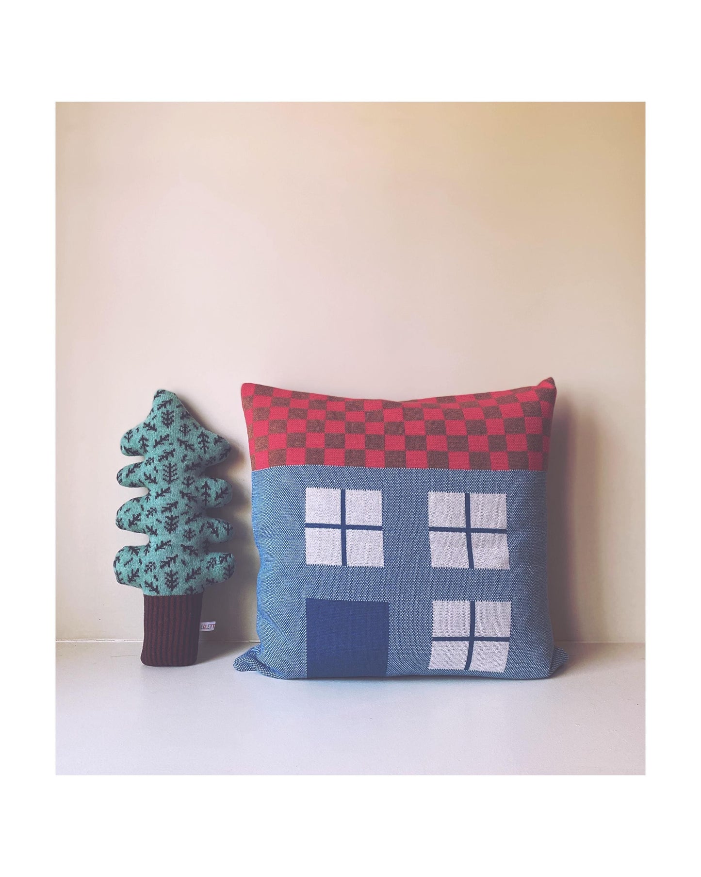 Decorative house shaped pillow and knitted tree plush on a white surface