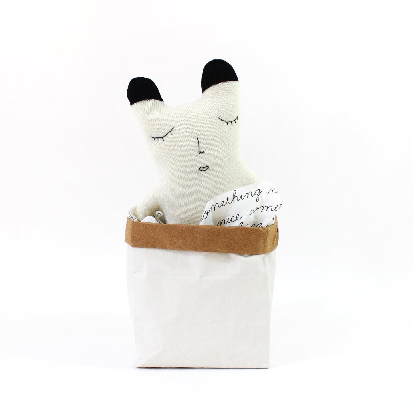 White knitted polar bear plush toy with black accents in a brown bag on a white background