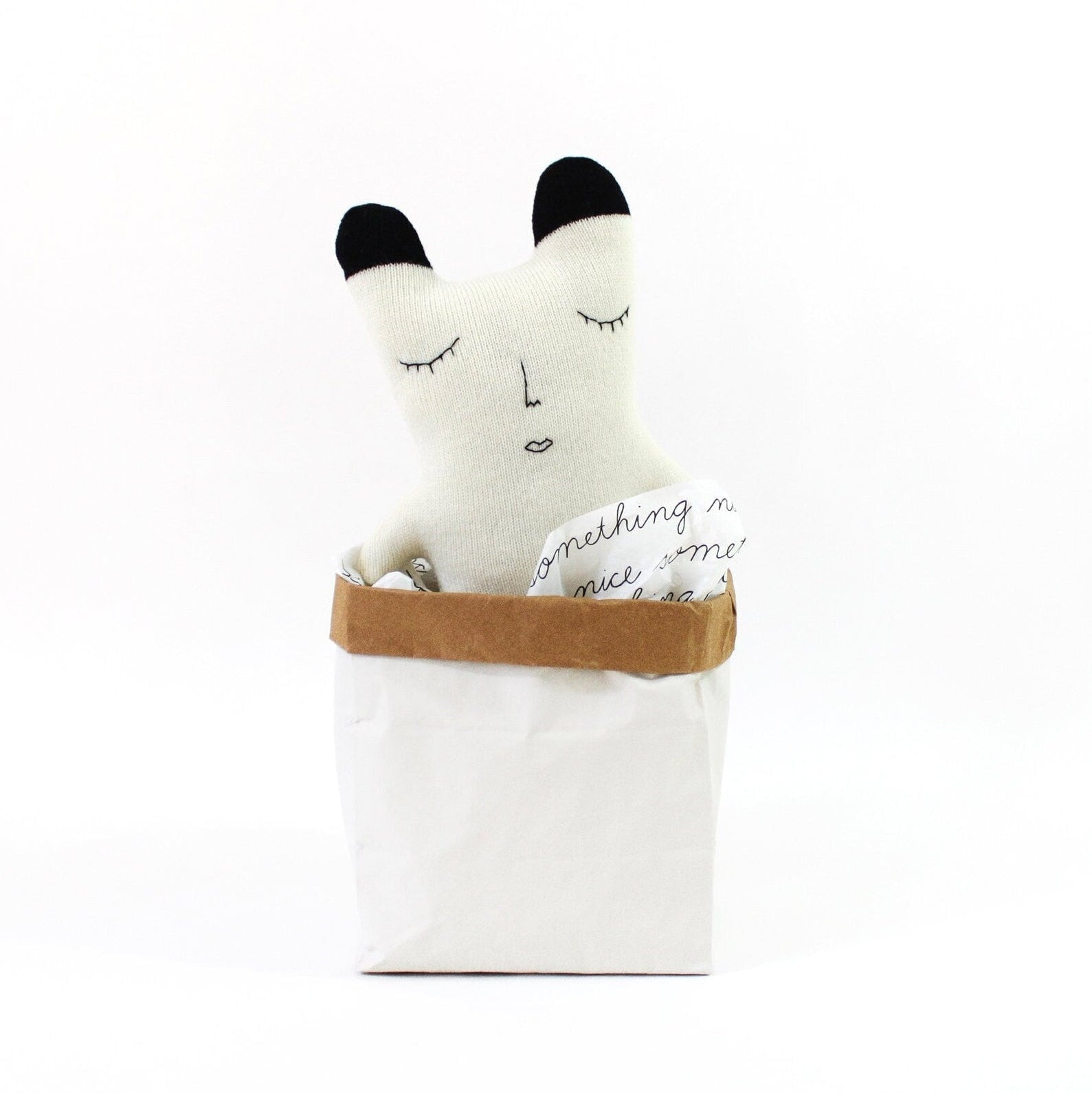 White knitted polar bear plush toy with black accents in a brown bag on a white background