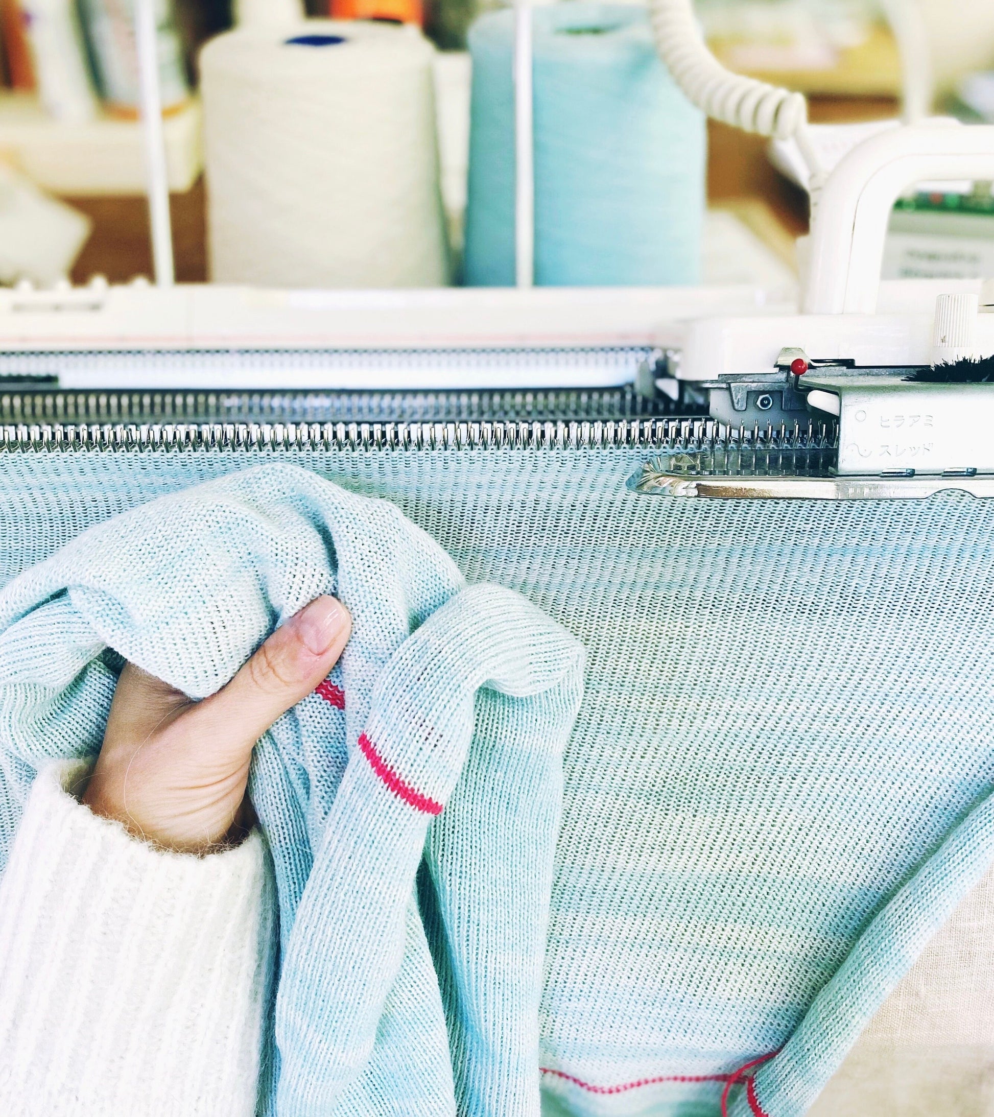 Hand holding fabric next to a knitting machine in a workshop setting