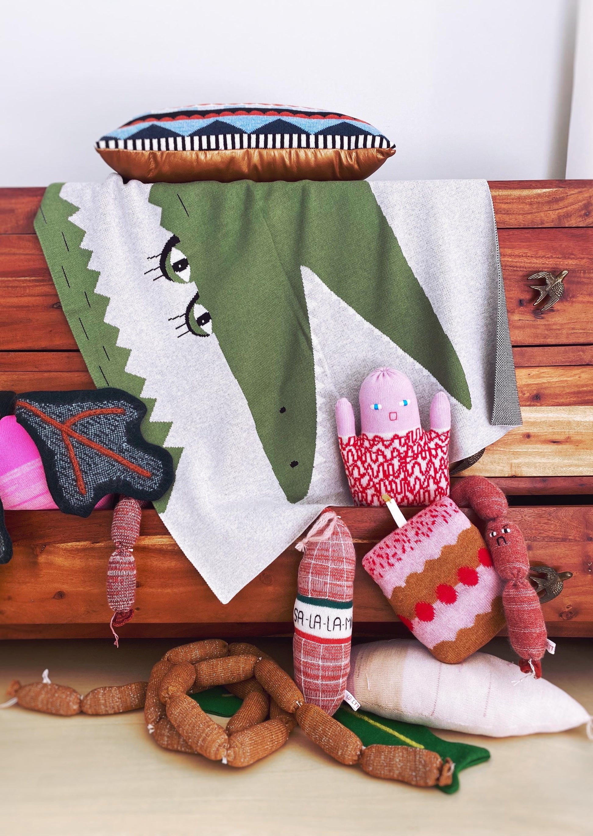 Collection of soft knitted lambswool toys on a wooden surface with a white towel draped over a green toy.