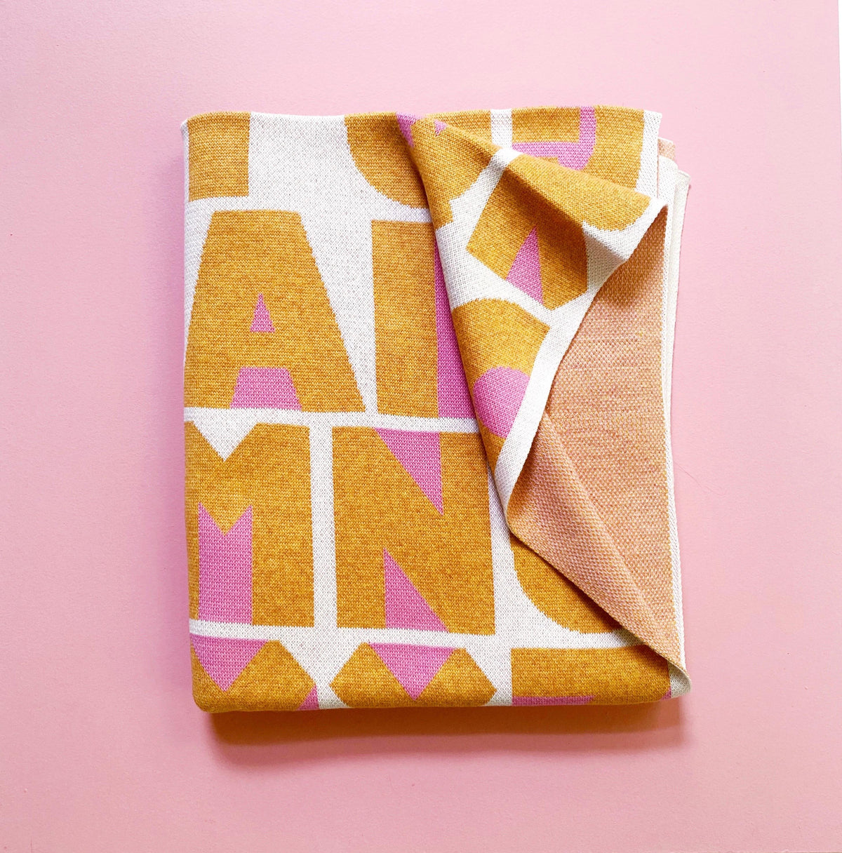 Folded knitted blanket with geometric pattern of colorful alphabet letters on a pink background