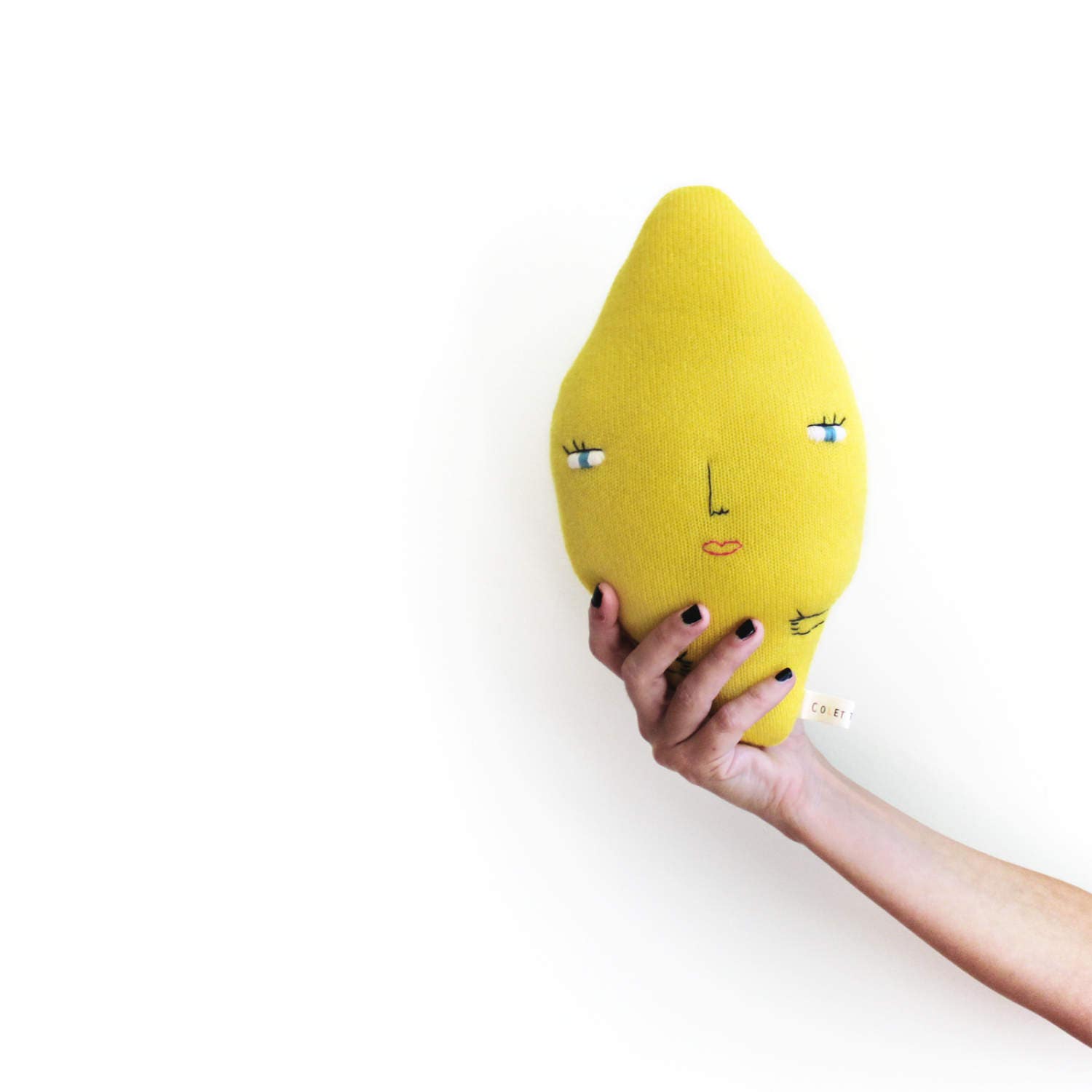 Hand holding a yellow lemon-shaped pillow with facial features on a white background