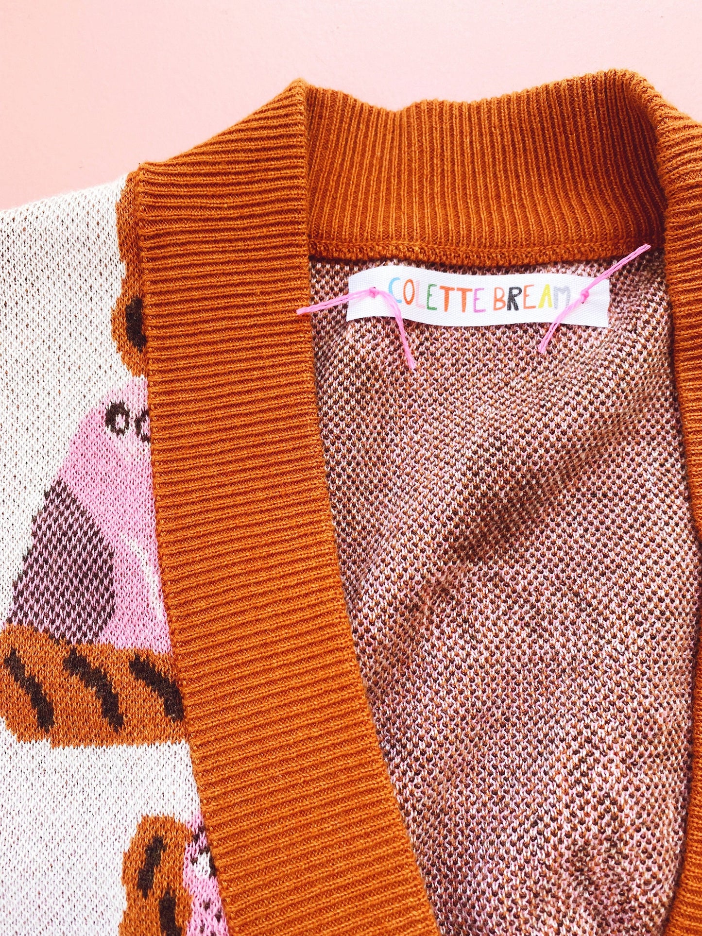 Close-up of a knitted orange V-neck sweater with a brand label on a pink background
