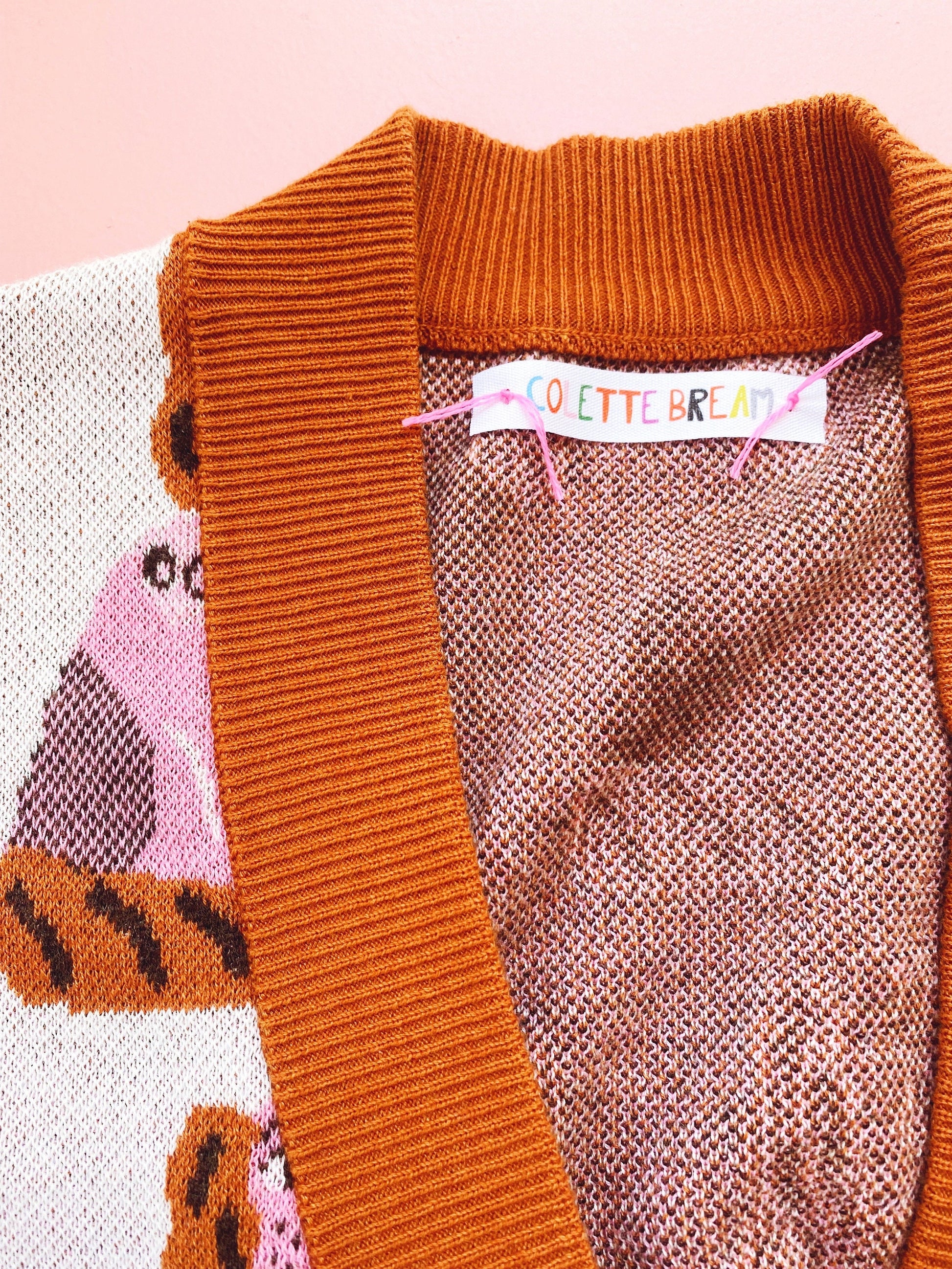 Close-up of a knitted orange V-neck sweater with a brand label on a pink background