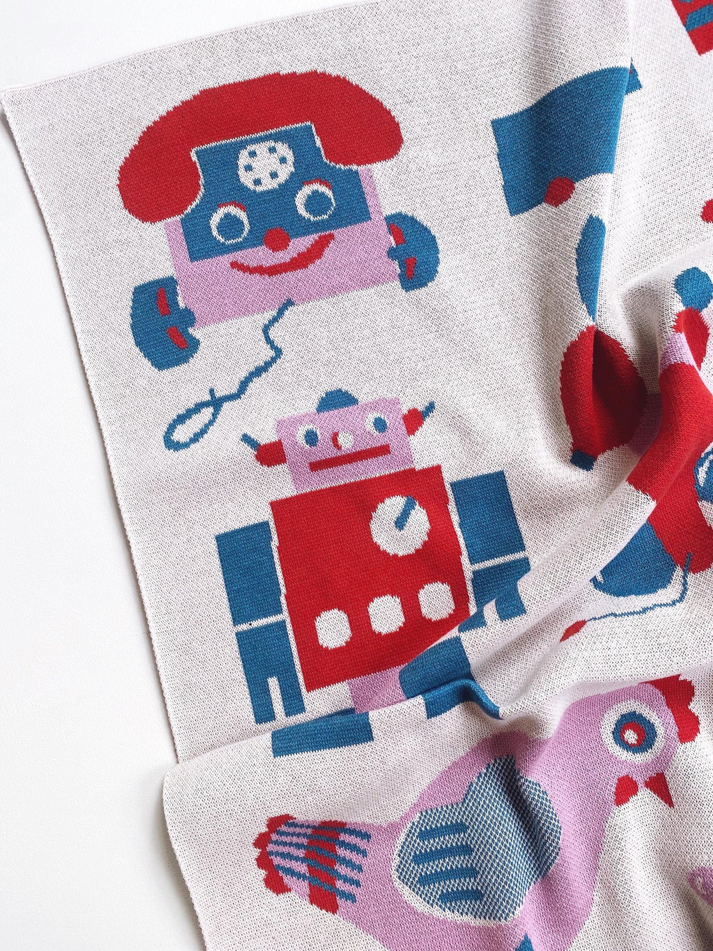 Knitted blanket with robot pattern and other vintage toy designs on a white background