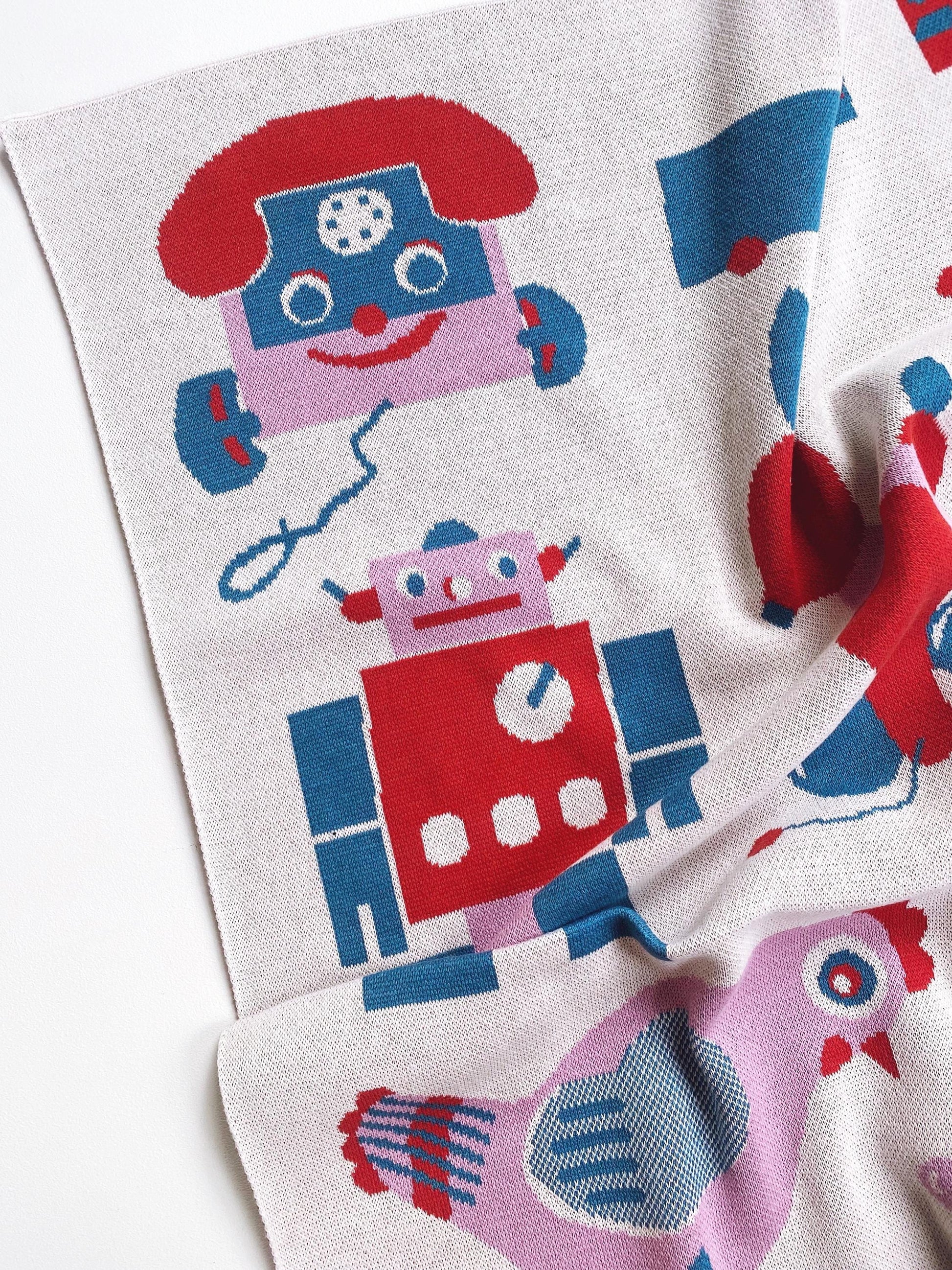 Knitted blanket with robot pattern and other vintage toy designs on a white background