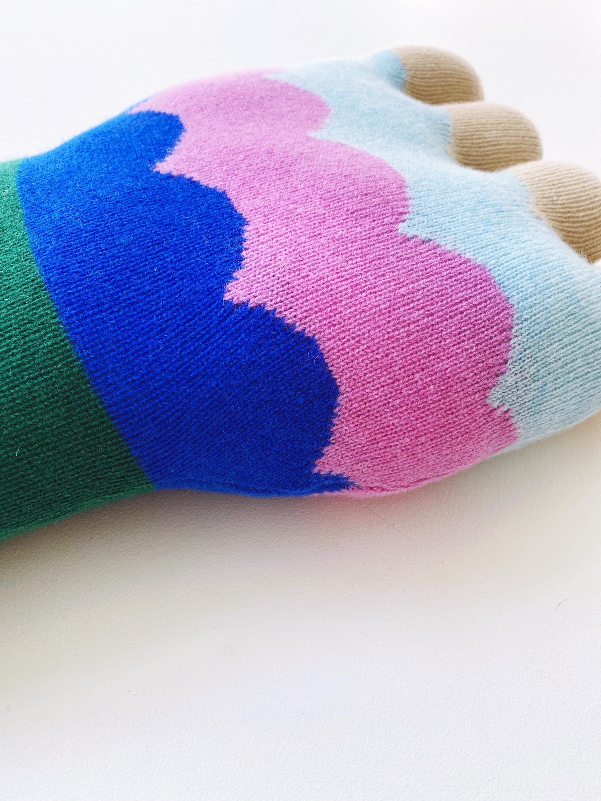 Colorful flower shaped pillow with blue, pink, green, and beige sections on a white background