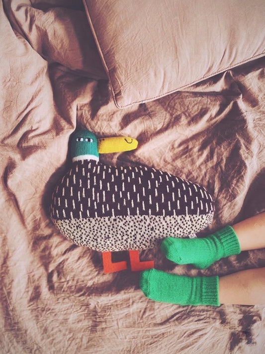 Soft knit lambsool toy duck with green feet on a bed