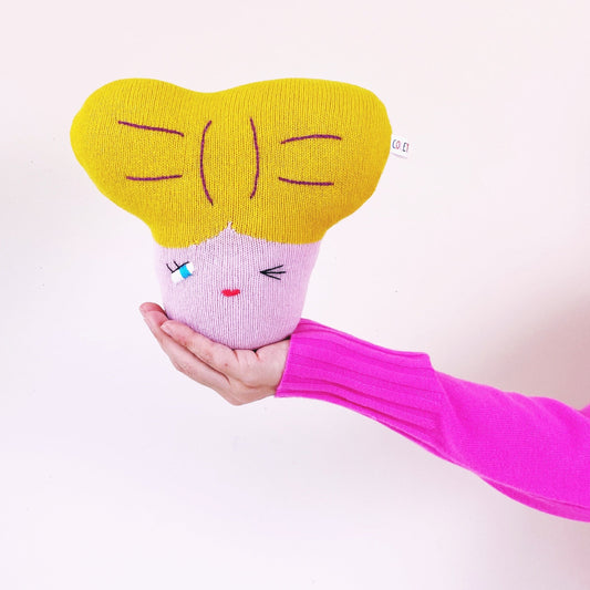 Hand holding a pink and yellow plush toy with a face on a white background