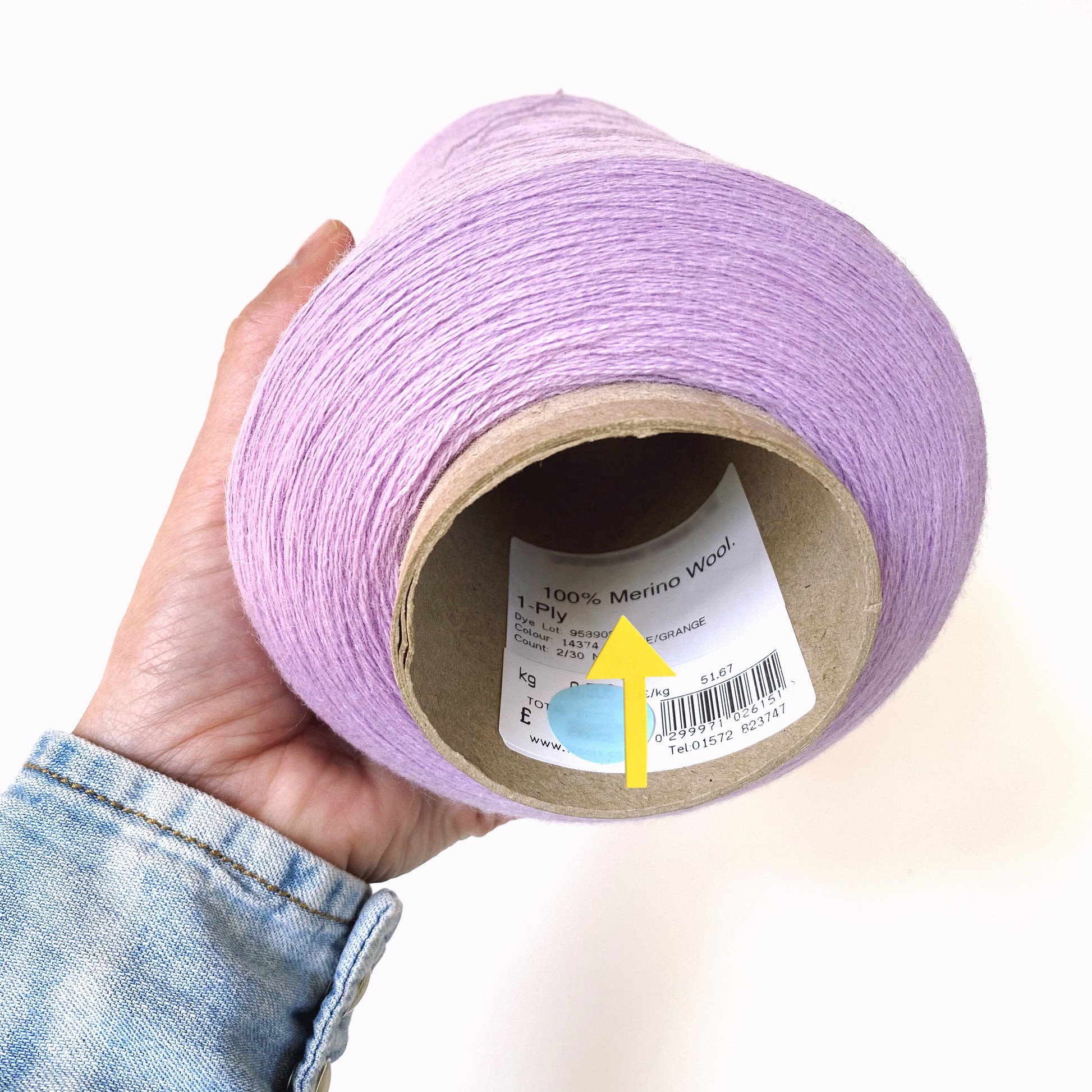 Hand holding a roll of purple yarn with a label on a white background