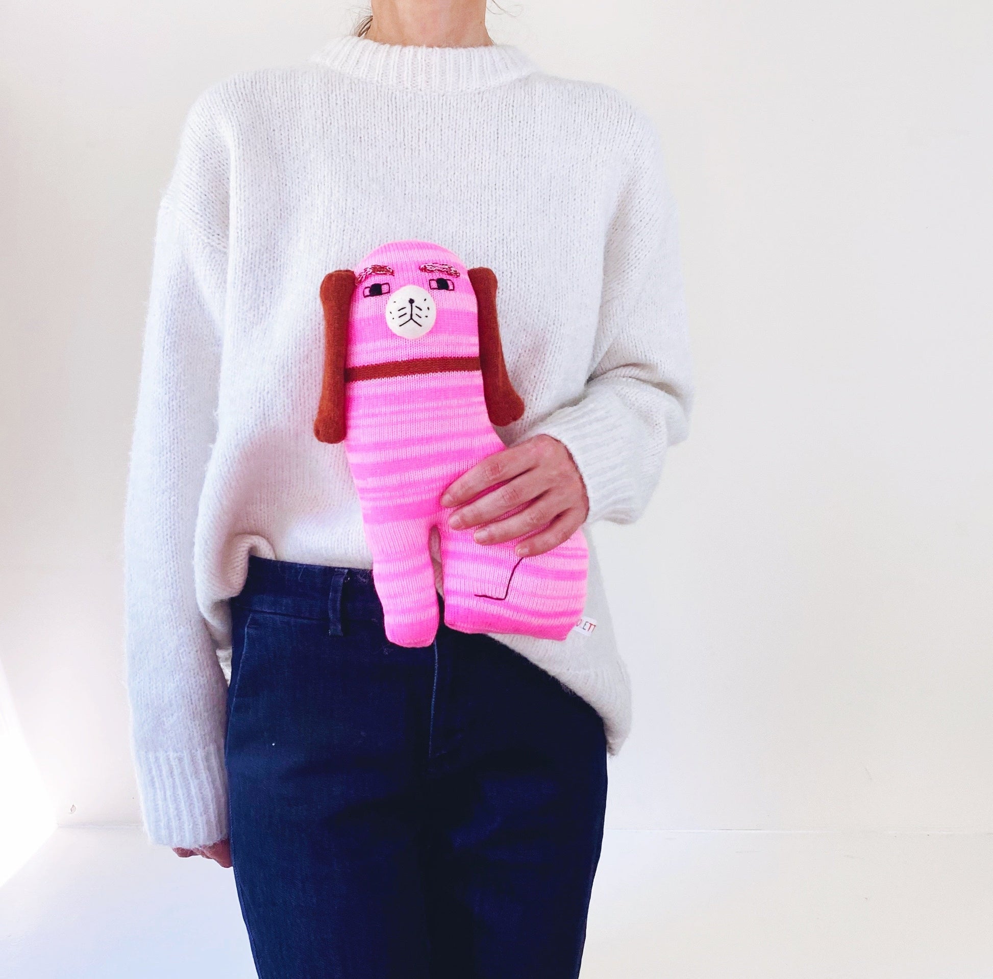 Person holding a pink knitted Staffordshire plush toy with a white background