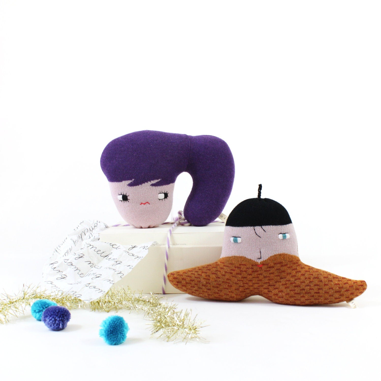 Two plush toys resembling a purple character with a large head and a white character with a brown beard  on a white background.