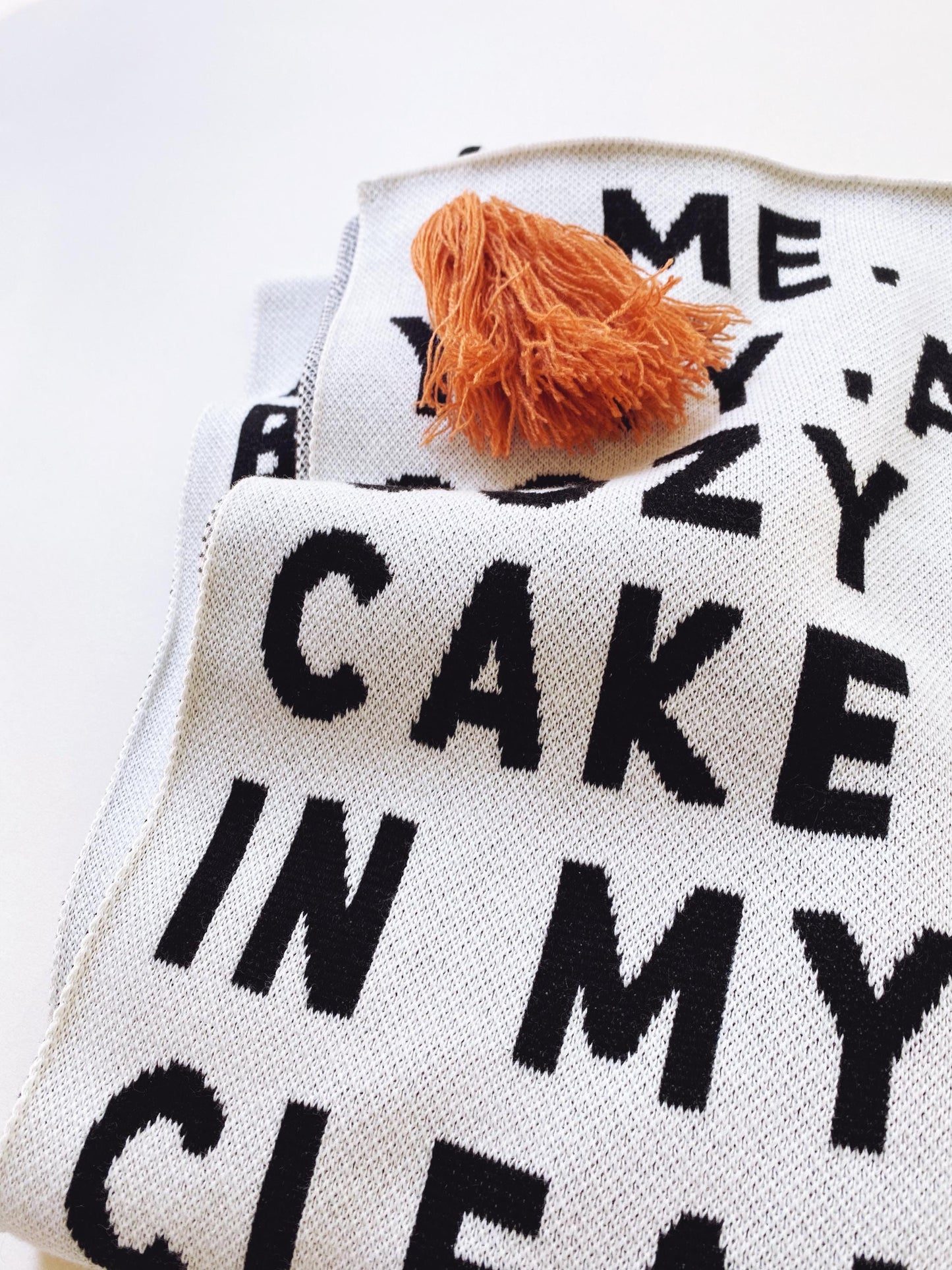 Detail of a knitted blanket throw with black and white text pattern and a tassel on a white background
