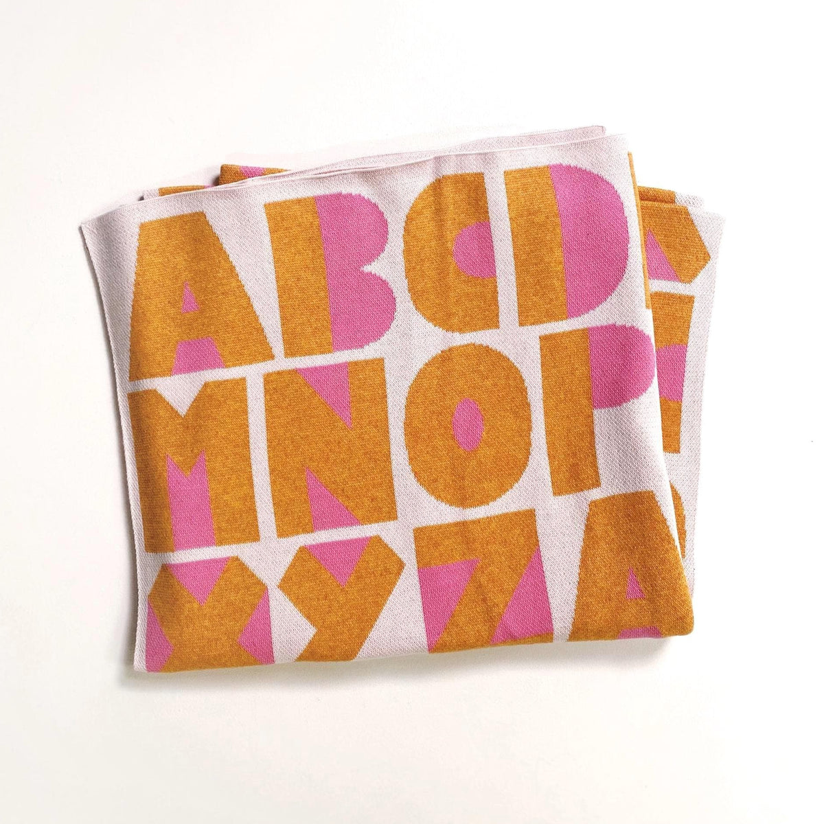 Folded knit blanket with yellow and pink alphabet letter pattern on a white background