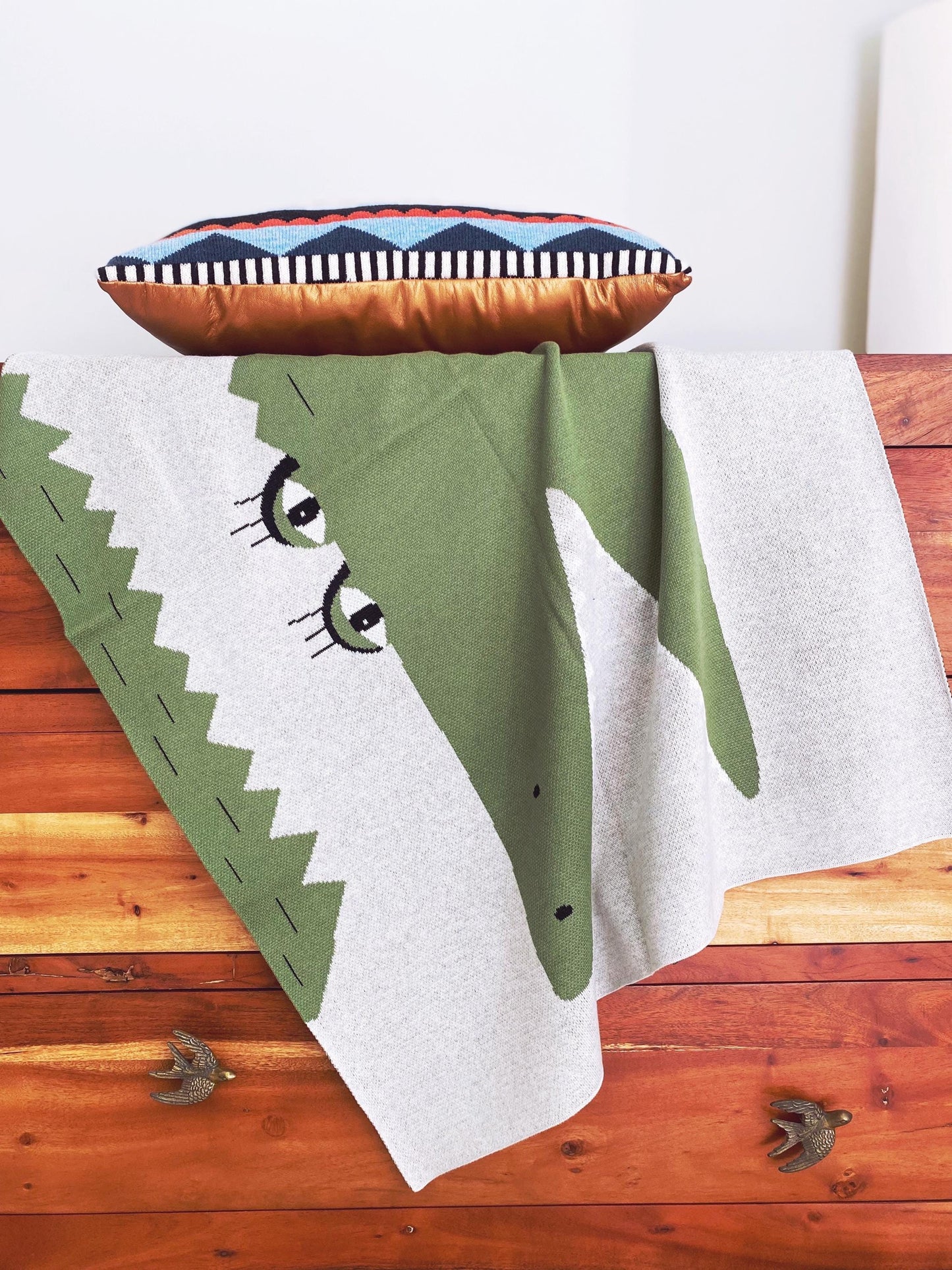 Green alligator blanket with a colorful pillow on a wooden dresser
