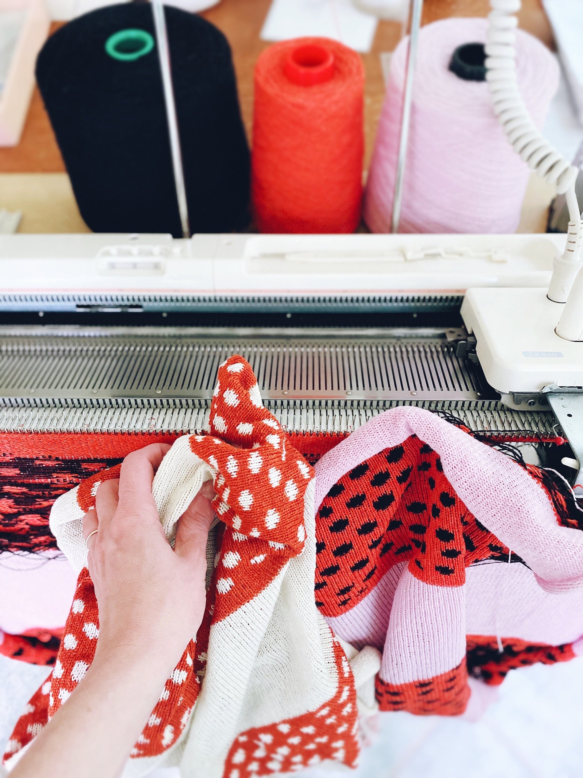 Knitting machine with colorful yarn and a hand holding a knitted item.